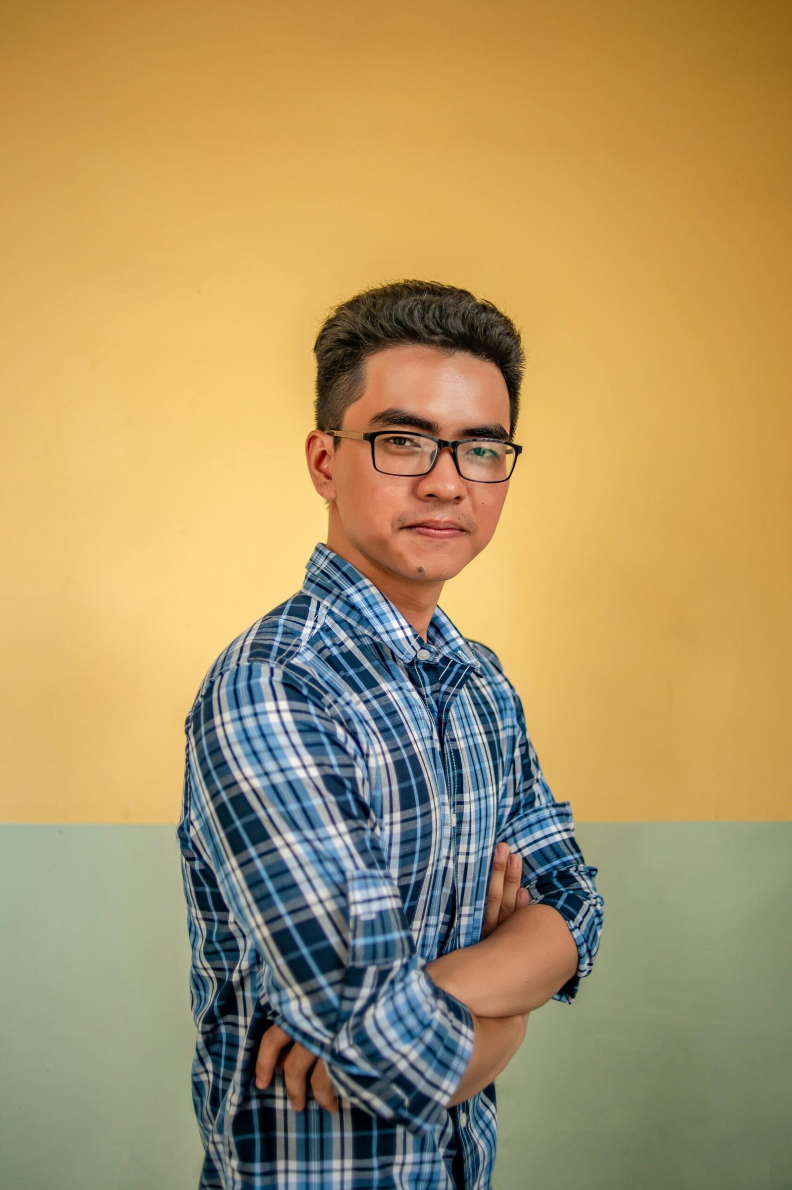 A portrait of a confident young man in glasses wearing a plaid shirt against a neutral background.